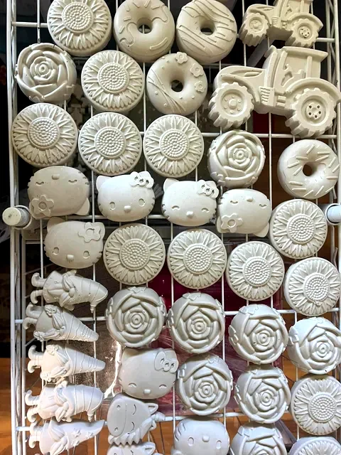 Paintable flower, character, tractor, and rose pieces drying on a rack